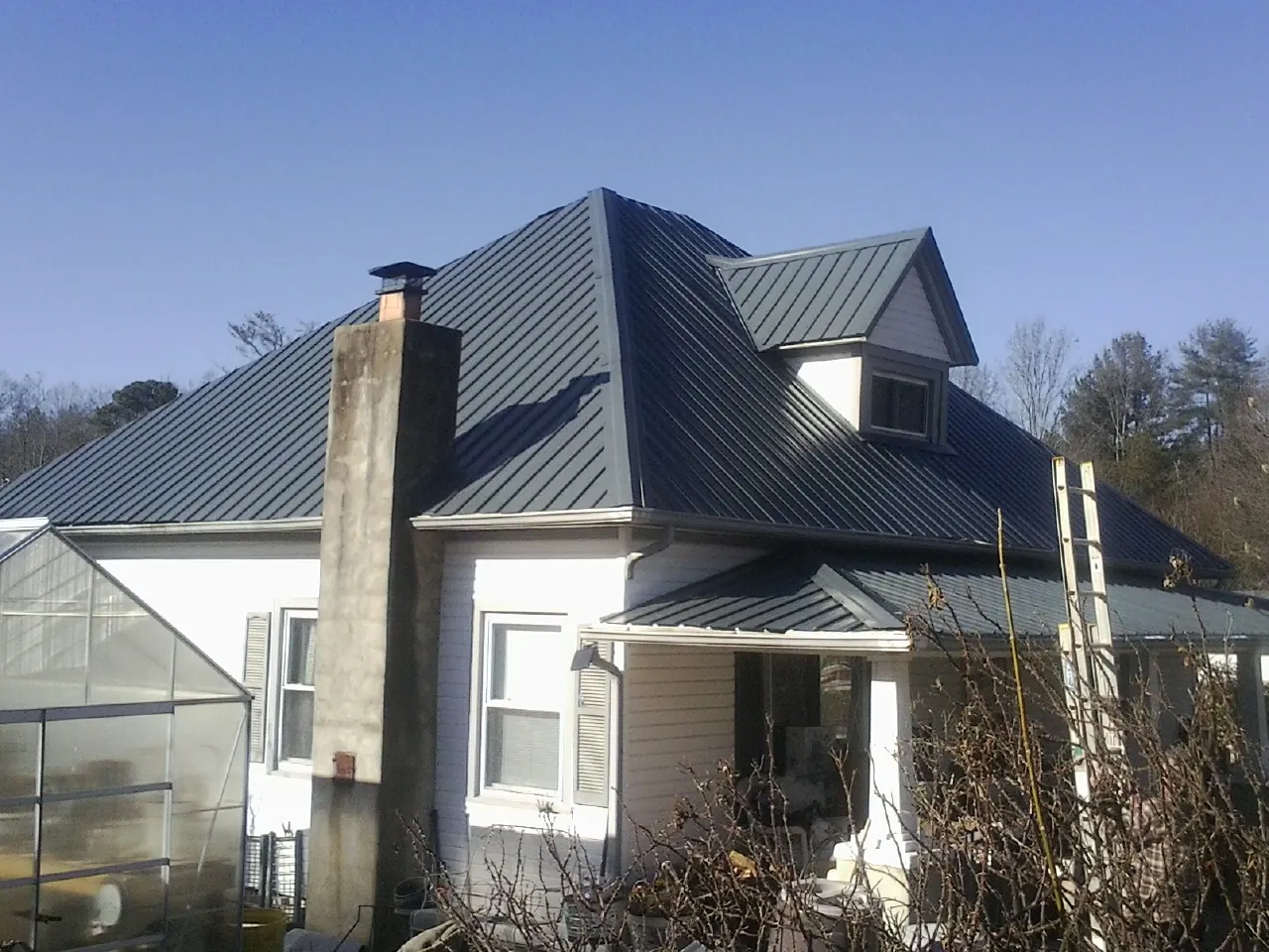Dark blue standing seam metal roof on a white farmhouse with dormer — Slate & Tile Roof Repair by Roofing Brothers in Cramerton