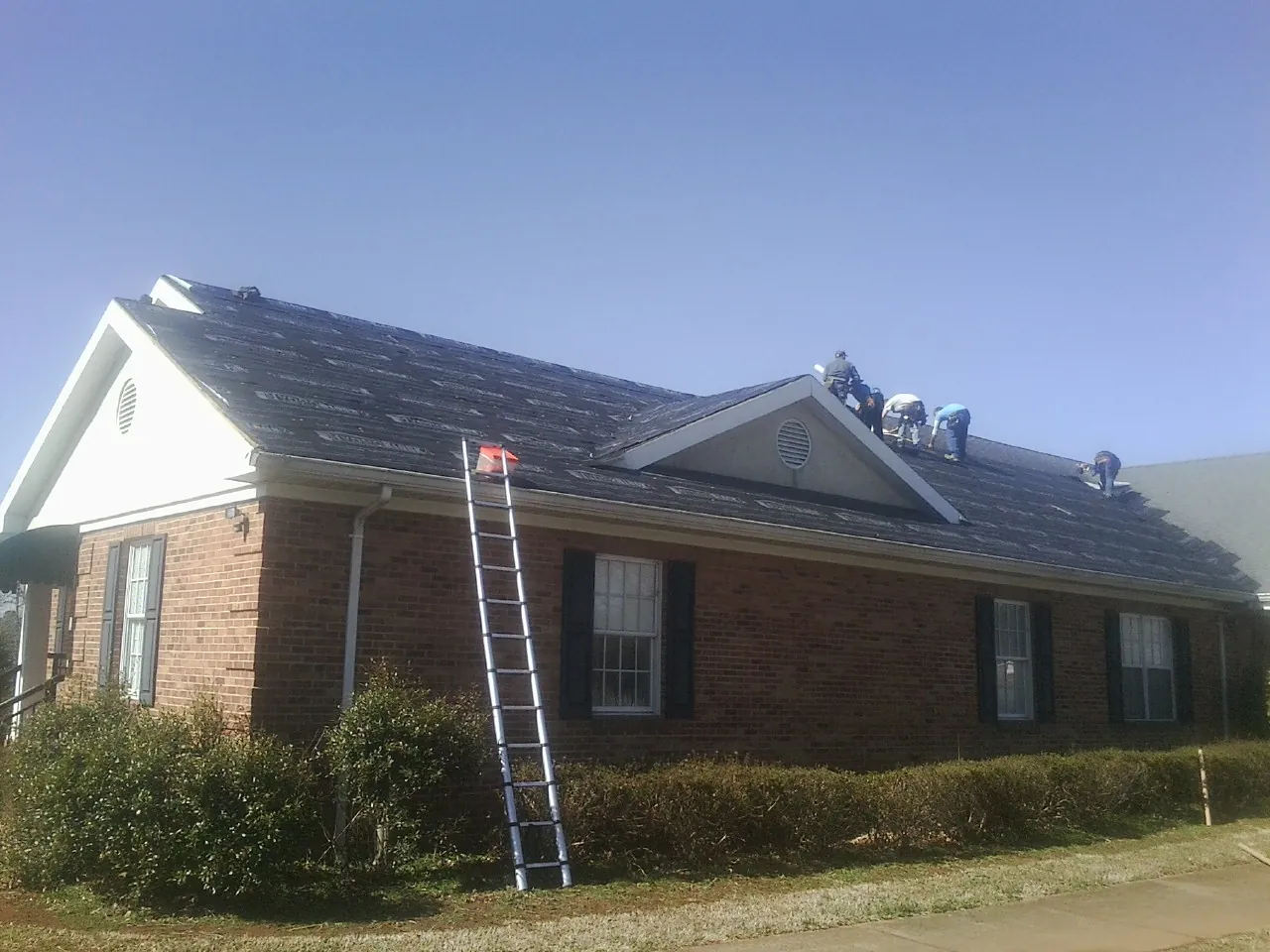 Crew tearing shingles off a brick ranch roof with a ladder set — Metal Roof Repair work by our crew in Cramerton