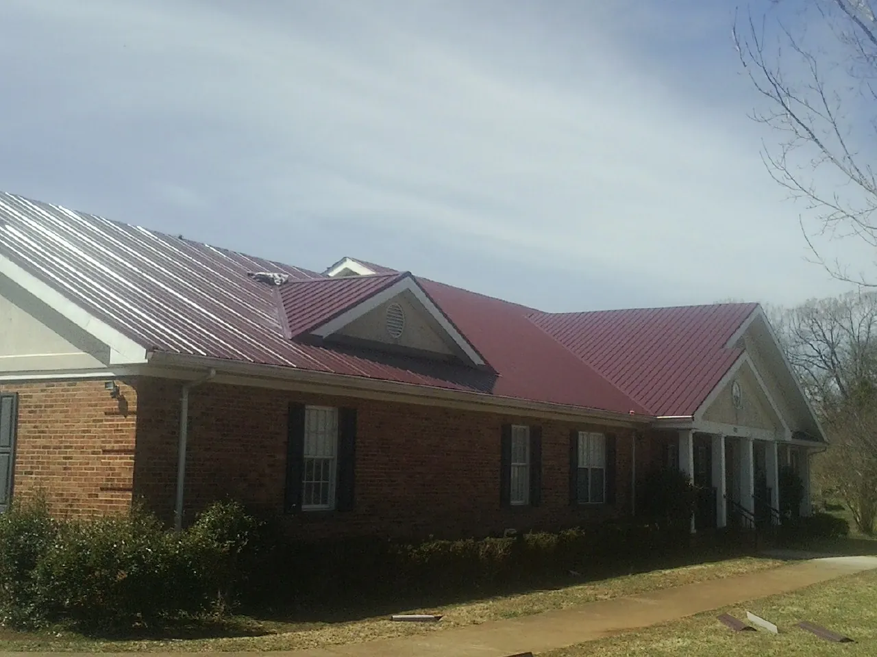 Red metal roof with gabled entries on a long brick building, from a Hail Damage Roof Repair job in Cramerton