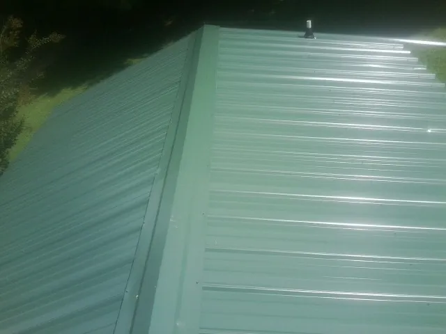 New green metal panels meeting at the ridge of a roof — Flat Roof Repair work by our crew in Cramerton