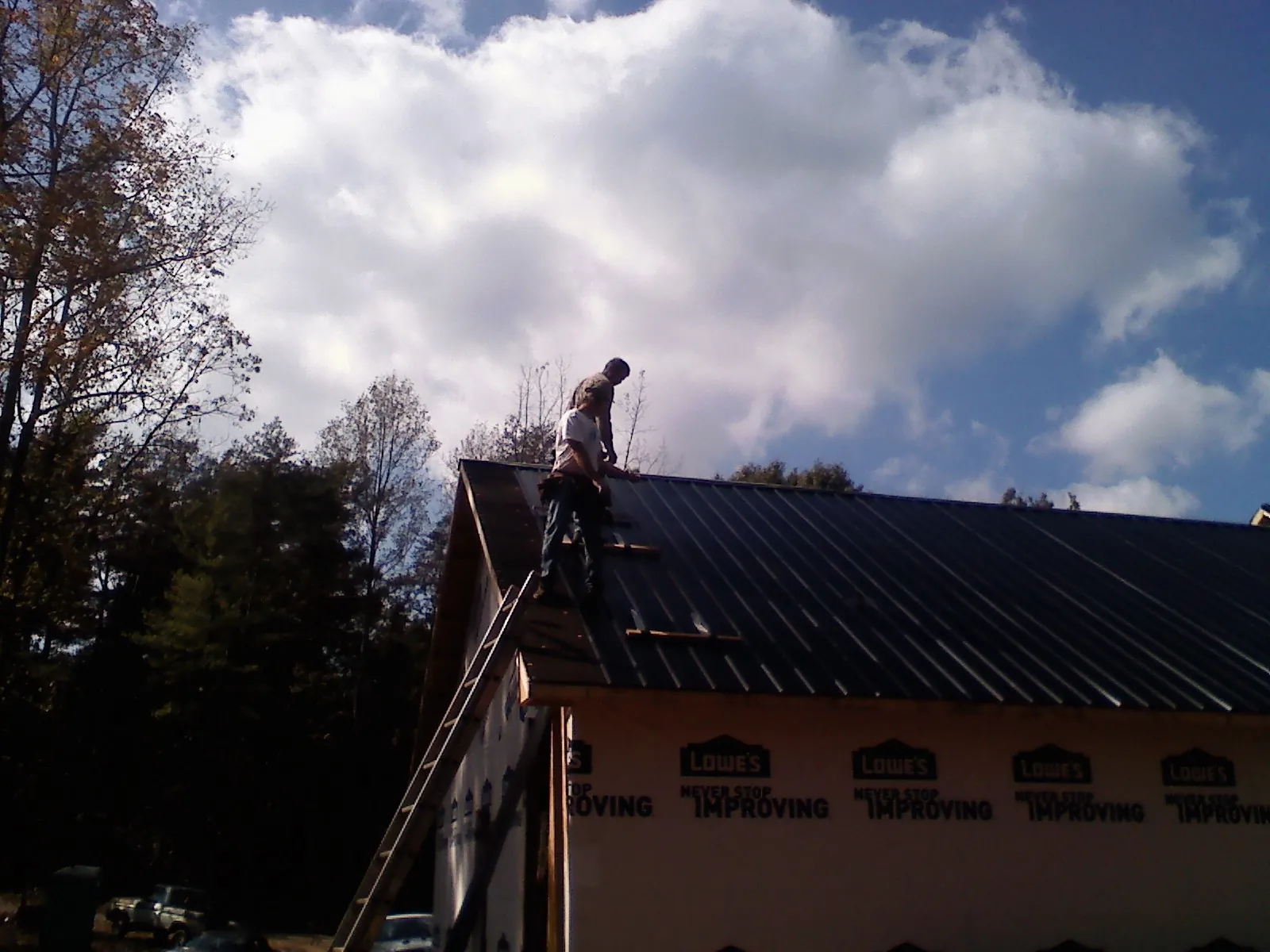Roofer fastening dark metal panels high against a cloudy sky, from a Roof Inspection job in Cramerton