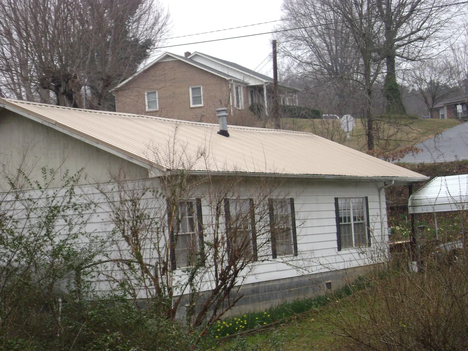 Tan metal roof on a white sided house set into a hillside — Commercial Roofing by Roofing Brothers in Cramerton